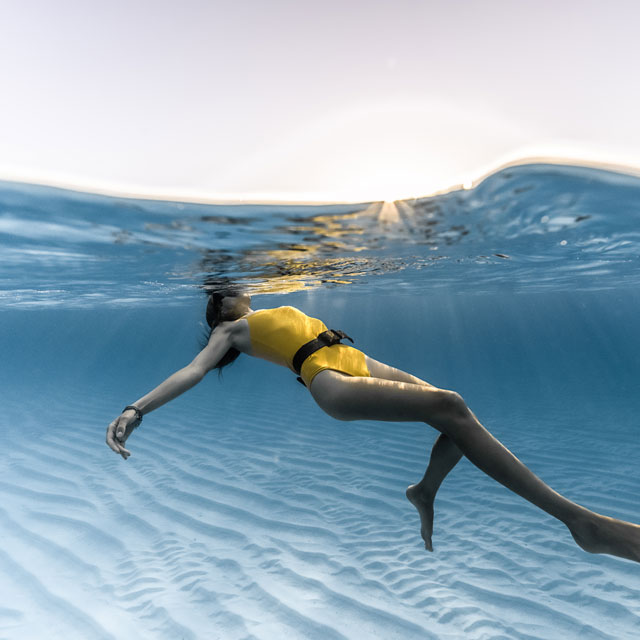 Woman in yellow swimsuit floating peacefully, half-underwater split shot